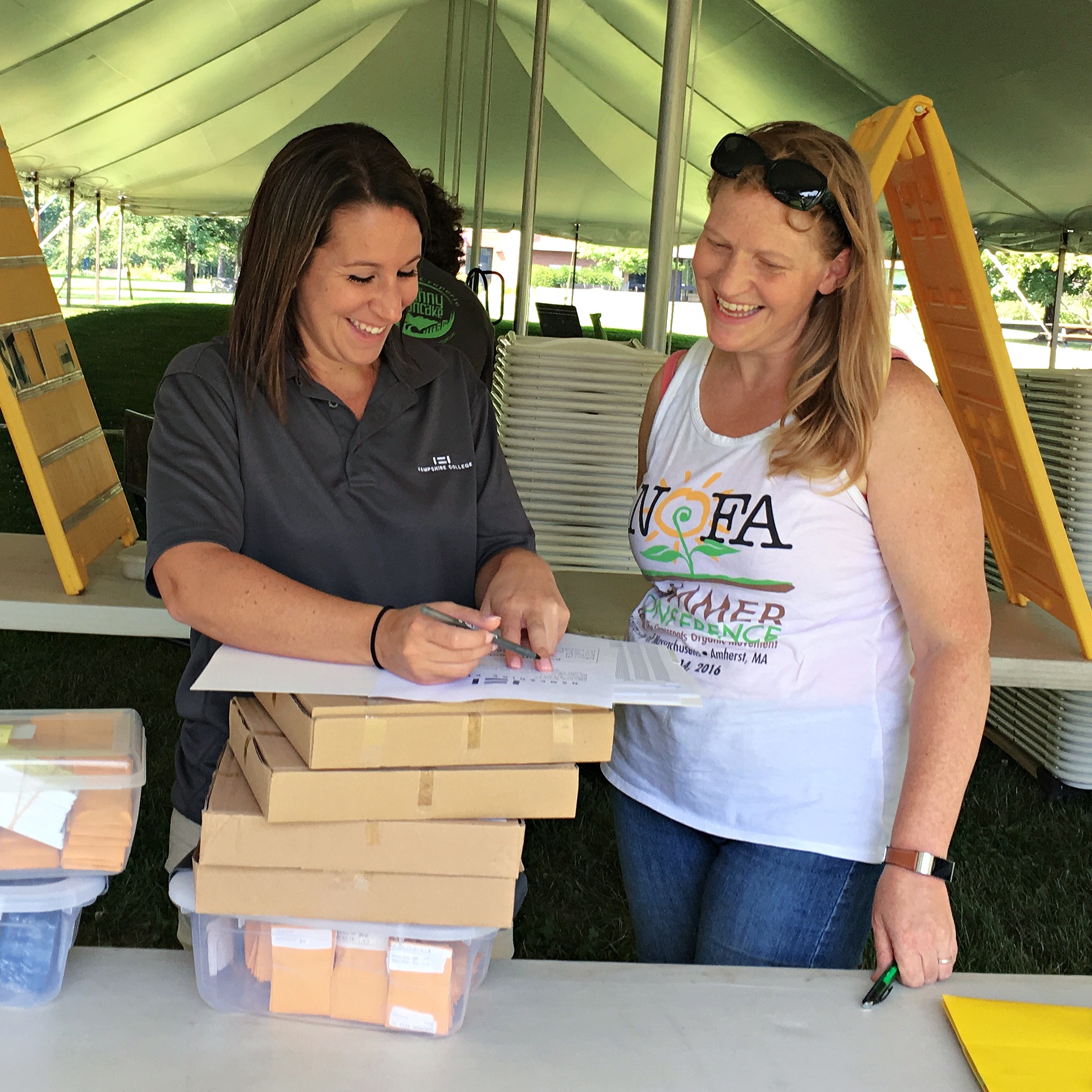 Two women stand under a tent signing papers